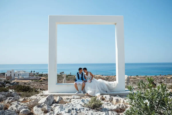 Genç gelin ve damat sahilde yürüyüş, Öpüşme ve sahip eğlenceli, düğün töreni kayalar ve deniz yakınında gülümseyen güzel. Kıbrıs Sahil düğün töreni