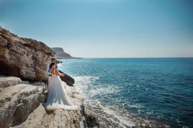 Genç gelin ve damat sahilde yürüyüş, Öpüşme ve sahip eğlenceli, düğün töreni kayalar ve deniz yakınında gülümseyen güzel. Kıbrıs Sahil düğün töreni