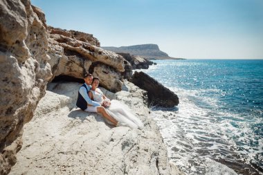Genç gelin ve damat sahilde yürüyüş, Öpüşme ve sahip eğlenceli, düğün töreni kayalar ve deniz yakınında gülümseyen güzel. Kıbrıs Sahil düğün töreni