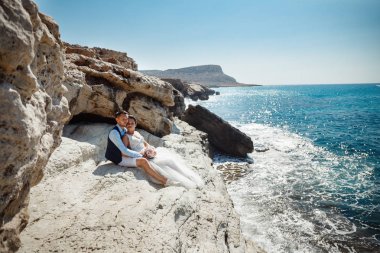 Genç gelin ve damat sahilde yürüyüş, Öpüşme ve sahip eğlenceli, düğün töreni kayalar ve deniz yakınında gülümseyen güzel. Kıbrıs Sahil düğün töreni