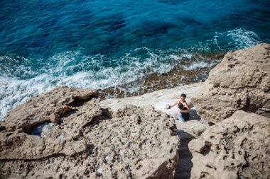 Genç gelin ve damat sahilde yürüyüş, Öpüşme ve sahip eğlenceli, düğün töreni kayalar ve deniz yakınında gülümseyen güzel. Kıbrıs Sahil düğün töreni