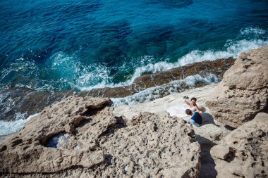 Genç gelin ve damat sahilde yürüyüş, Öpüşme ve sahip eğlenceli, düğün töreni kayalar ve deniz yakınında gülümseyen güzel. Kıbrıs Sahil düğün töreni