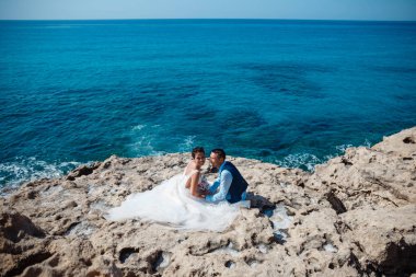 Genç gelin ve damat sahilde yürüyüş, Öpüşme ve sahip eğlenceli, düğün töreni kayalar ve deniz yakınında gülümseyen güzel. Kıbrıs Sahil düğün töreni