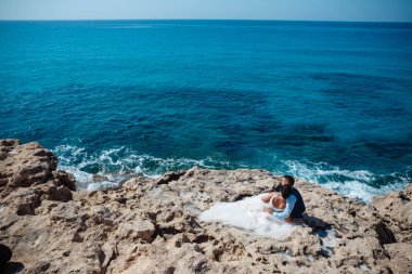 Genç gelin ve damat sahilde yürüyüş, Öpüşme ve sahip eğlenceli, düğün töreni kayalar ve deniz yakınında gülümseyen güzel. Kıbrıs Sahil düğün töreni