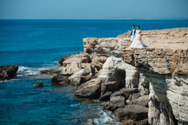 Genç gelin ve damat sahilde yürüyüş, Öpüşme ve sahip eğlenceli, düğün töreni kayalar ve deniz yakınında gülümseyen güzel. Kıbrıs Sahil düğün töreni