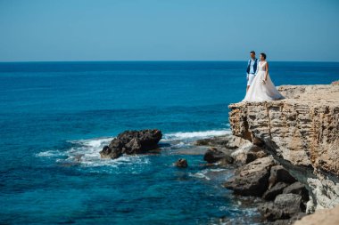Genç gelin ve damat sahilde yürüyüş, Öpüşme ve sahip eğlenceli, düğün töreni kayalar ve deniz yakınında gülümseyen güzel. Kıbrıs Sahil düğün töreni