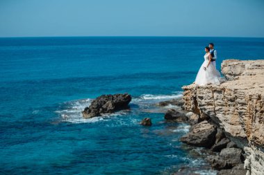 Genç gelin ve damat sahilde yürüyüş, Öpüşme ve sahip eğlenceli, düğün töreni kayalar ve deniz yakınında gülümseyen güzel. Kıbrıs Sahil düğün töreni