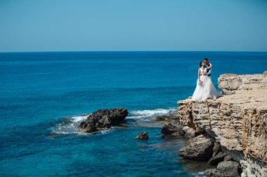 Genç gelin ve damat sahilde yürüyüş, Öpüşme ve sahip eğlenceli, düğün töreni kayalar ve deniz yakınında gülümseyen güzel. Kıbrıs Sahil düğün töreni
