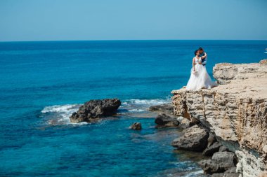 Genç gelin ve damat sahilde yürüyüş, Öpüşme ve sahip eğlenceli, düğün töreni kayalar ve deniz yakınında gülümseyen güzel. Kıbrıs Sahil düğün töreni