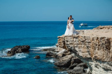 Genç gelin ve damat sahilde yürüyüş, Öpüşme ve sahip eğlenceli, düğün töreni kayalar ve deniz yakınında gülümseyen güzel. Kıbrıs Sahil düğün töreni