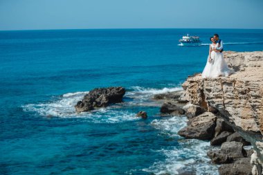 Genç gelin ve damat sahilde yürüyüş, Öpüşme ve sahip eğlenceli, düğün töreni kayalar ve deniz yakınında gülümseyen güzel. Kıbrıs Sahil düğün töreni
