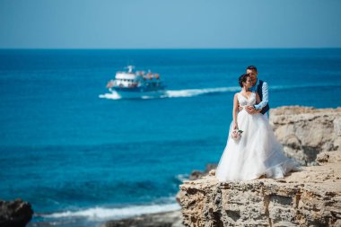 Genç gelin ve damat sahilde yürüyüş, Öpüşme ve sahip eğlenceli, düğün töreni kayalar ve deniz yakınında gülümseyen güzel. Kıbrıs Sahil düğün töreni