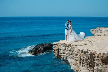 Genç gelin ve damat sahilde yürüyüş, Öpüşme ve sahip eğlenceli, düğün töreni kayalar ve deniz yakınında gülümseyen güzel. Kıbrıs Sahil düğün töreni