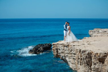 Genç gelin ve damat sahilde yürüyüş, Öpüşme ve sahip eğlenceli, düğün töreni kayalar ve deniz yakınında gülümseyen güzel. Kıbrıs Sahil düğün töreni