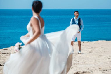 Genç gelin ve damat sahilde yürüyüş, Öpüşme ve sahip eğlenceli, düğün töreni kayalar ve deniz yakınında gülümseyen güzel. Kıbrıs Sahil düğün töreni