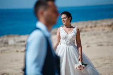 Genç gelin ve damat sahilde yürüyüş, Öpüşme ve sahip eğlenceli, düğün töreni kayalar ve deniz yakınında gülümseyen güzel. Kıbrıs Sahil düğün töreni