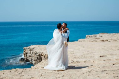 Genç gelin ve damat sahilde yürüyüş, Öpüşme ve sahip eğlenceli, düğün töreni kayalar ve deniz yakınında gülümseyen güzel. Kıbrıs Sahil düğün töreni