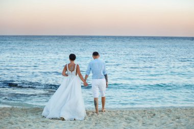 Genç gelin ve damat sahilde yürüyüş, Öpüşme ve sahip eğlenceli, düğün töreni kayalar ve deniz yakınında gülümseyen güzel. Kıbrıs Sahil düğün töreni