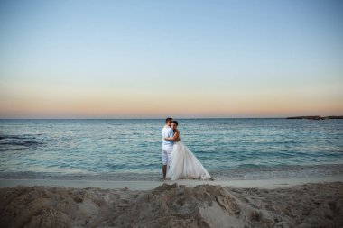 Genç gelin ve damat sahilde yürüyüş, Öpüşme ve sahip eğlenceli, düğün töreni kayalar ve deniz yakınında gülümseyen güzel. Kıbrıs Sahil düğün töreni