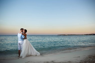 Genç gelin ve damat sahilde yürüyüş, Öpüşme ve sahip eğlenceli, düğün töreni kayalar ve deniz yakınında gülümseyen güzel. Kıbrıs Sahil düğün töreni