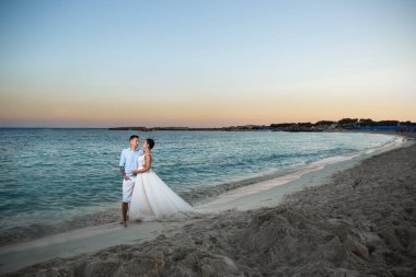 Genç gelin ve damat sahilde yürüyüş, Öpüşme ve sahip eğlenceli, düğün töreni kayalar ve deniz yakınında gülümseyen güzel. Kıbrıs Sahil düğün töreni