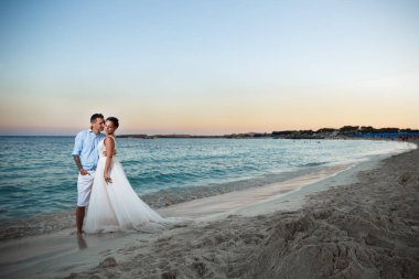 Genç gelin ve damat sahilde yürüyüş, Öpüşme ve sahip eğlenceli, düğün töreni kayalar ve deniz yakınında gülümseyen güzel. Kıbrıs Sahil düğün töreni