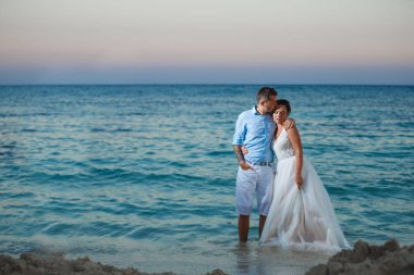 Genç gelin ve damat sahilde yürüyüş, Öpüşme ve sahip eğlenceli, düğün töreni kayalar ve deniz yakınında gülümseyen güzel. Kıbrıs Sahil düğün töreni