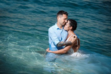 Genç gelin ve damat sahilde yürüyüş, Öpüşme ve sahip eğlenceli, düğün töreni kayalar ve deniz yakınında gülümseyen güzel. Kıbrıs Sahil düğün töreni