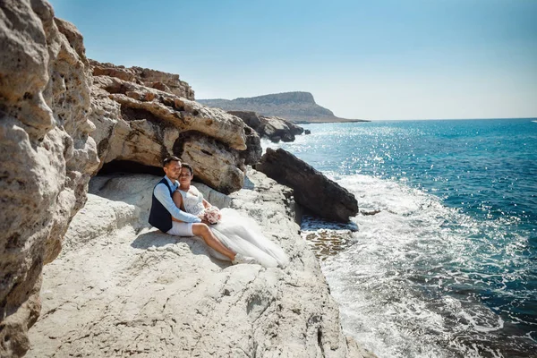 Genç gelin ve damat sahilde yürüyüş, Öpüşme ve sahip eğlenceli, düğün töreni kayalar ve deniz yakınında gülümseyen güzel. Kıbrıs Sahil düğün töreni
