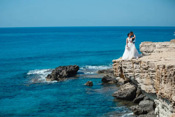 Genç gelin ve damat sahilde yürüyüş, Öpüşme ve sahip eğlenceli, düğün töreni kayalar ve deniz yakınında gülümseyen güzel. Kıbrıs Sahil düğün töreni