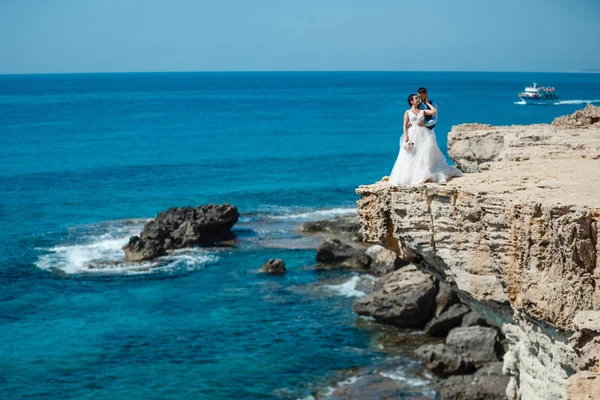 Genç gelin ve damat sahilde yürüyüş, Öpüşme ve sahip eğlenceli, düğün töreni kayalar ve deniz yakınında gülümseyen güzel. Kıbrıs Sahil düğün töreni