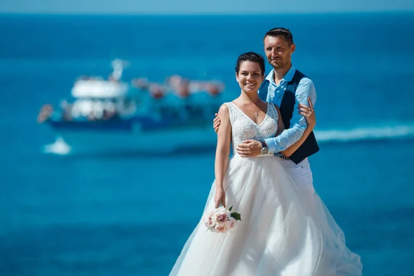 美丽的微笑的年轻新娘和新郎走在海滩上 亲吻和乐趣 婚礼附近的岩石和大海 塞浦路斯海岸的婚礼仪式 — 图库照片