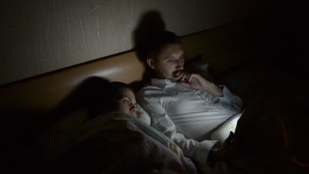 年轻的一对夫妇带着智能手机和平板电脑 深夜在家里躺在床上 — 图库视频影像