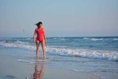 Kırmızı bir mayo içinde sahilde poz güzel mutlu esmer kız.