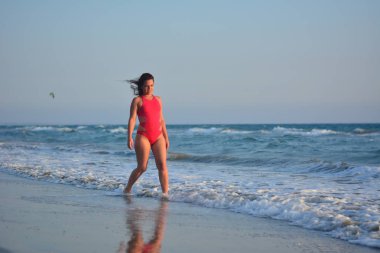 Kırmızı bir mayo içinde sahilde poz güzel mutlu esmer kız.