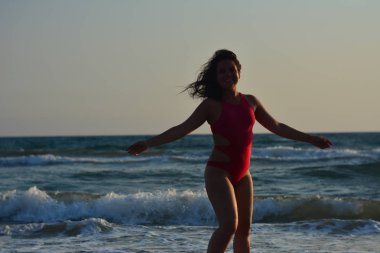 Kırmızı bir mayo içinde sahilde poz güzel mutlu esmer kız.