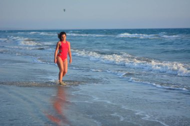 Kırmızı bir mayo içinde sahilde poz güzel mutlu esmer kız.