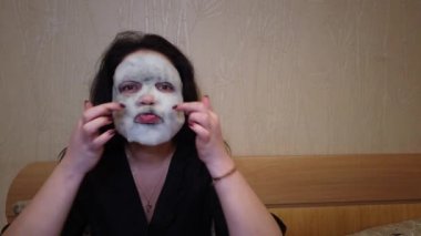 Kadın yatakta yüzündeki akşamları kağıt maske uygulamak