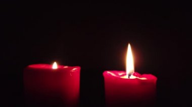Karanlık arka planda titreşen alev ile kırmızı mum yakma.