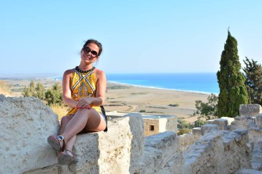 Kız deniz ve dağların güzel bir görünümü ile eski bir ağacın altında bir uçurumun üzerinde oturur. Avrupa beldesinde tatil. Seyahat ve eğlence.