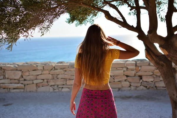 La ragazza si siede su una scogliera sotto un vecchio albero con una splendida vista sul mare e sulle montagne. Vacanze nella località europea. Viaggi e tempo libero . — Foto Stock