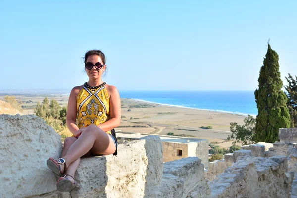 La chica se sienta en un acantilado bajo un viejo árbol con una hermosa vista del mar y las montañas. Vacaciones en el resort europeo. Viajes y ocio . — Foto de Stock