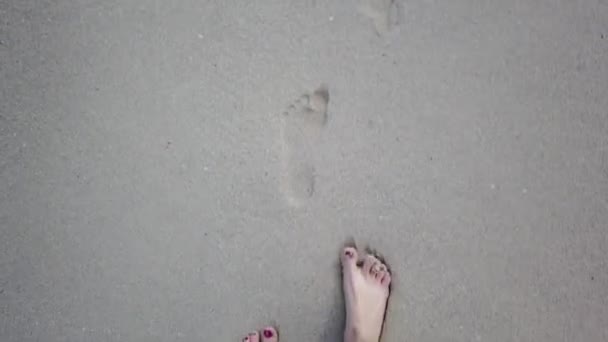 Pohled mladé ženy, jak šlapu po zlatém písku na mořské pláži. Ženský nohy chodí blízko oceánu. Holá noha dívky na písečném břehu s vlnami. Letní dovolená nebo dovolená