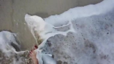 Deniz plajındaki altın kuma basan genç kadının bakış açısı. Okyanus kenarında yürüyen dişi bacaklar. Dalgalarla kumlu kıyıya çıkan kızın çıplak ayağı. Yaz tatili veya tatil
