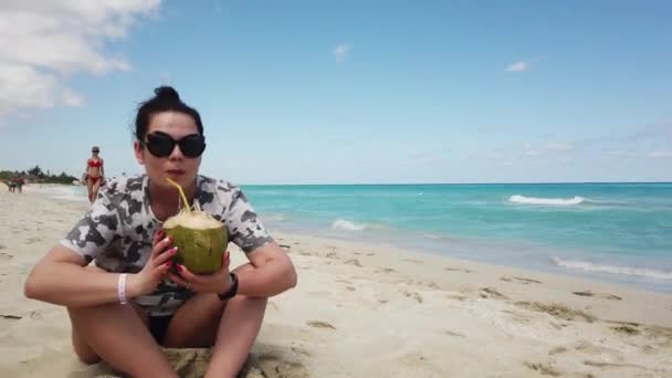 一个美丽的可爱布鲁内特年轻女子或一个快乐的女孩的肖像 在阳光下喝椰子 在热带海滩的风 概念海波放松在海边在夏天 巴拉德罗 — 图库视频影像