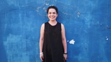 Kız duyguları gösterir. Kar beyazı gülümsemesi olan genç güzel bir kadın, mavi bir duvarın arka planına karşı pozlar.