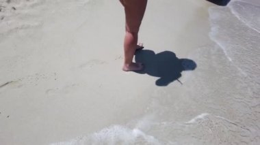 Kadın ayaklar arka planda okyanus dalgaları ile plajda altın kum üzerinde yürüyor. Genç kadının bacakları kuma basıyor. Deniz kıyısında yalınayak kız. Yaz tatili tatili. Yavaş hareket yakın çekim