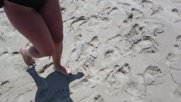 海の波が背景にビーチで金色の砂の上を歩いている女性の足 砂の上を踏んでいる若い女性の脚 海岸で裸足の女の子 夏休みの休日 スローモーションのクローズアップ — ストック動画