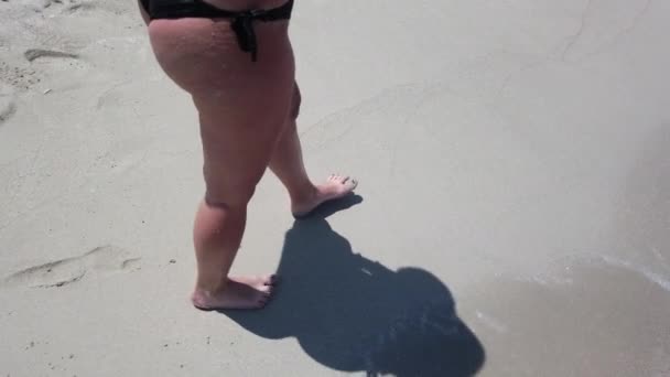 海の波が背景にビーチで金色の砂の上を歩いている女性の足 砂の上を踏んでいる若い女性の脚 海岸で裸足の女の子 夏休みの休日 スローモーションのクローズアップ — ストック動画