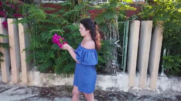 Giovane donna bruna attraente cammina sullo sfondo di fiori rossi primaverili nel parco. Ragazza con fiori rossi tra le mani . — Video Stock